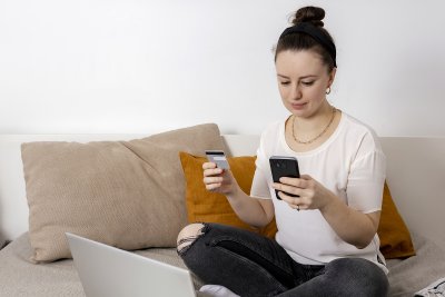 young woman with debit card and phone in front of computer
